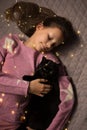 A teenage girl lies on a bed with a black cat wrapped in a garland, top view Royalty Free Stock Photo
