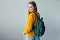 Teenage girl looking at camera and smiles. Beautiful student girl standing in yellow sweater and blue jeans and green backpack dre