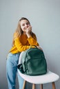 Teenage girl looks at camera .lean on hand and white modern chair with leather rucksacks. Beautiful girl in yellow sweater and blu