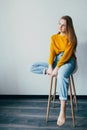 Teenage girl looks at left side.sitting on white modern chair with one  leg raise up. Beautiful girl in yellow sweater and blue je Royalty Free Stock Photo