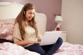 Teenage Girl Lying On Bed Using Laptop Wearing Headphones Royalty Free Stock Photo