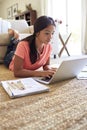 Teenage girl lying on the floor in the living room doing her homework using a laptop computer, low angle, close up, vertical Royalty Free Stock Photo