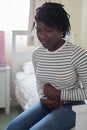 Teenage Girl In Pain Clutching Stomach In Bedroom