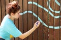 A teenage girl paints with a brush on a brown fence