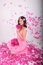 Teenage girl in pink dress with bouquet of peonies sitting in rain of petals