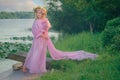 A teenage girl in a pink dress and a wreath of flowers on her head stands by the river. Summer. Nature. Inspiration Royalty Free Stock Photo