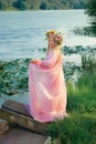 A teenage girl in a pink dress and a wreath of flowers on her head stands by the river. Summer. Nature. Inspiration Royalty Free Stock Photo