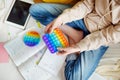 Teenage girl playing with rainbow pop-it fidget toy while studying at home. Teen kid with trendy stress and anxiety relief