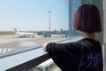 Teenage girl with purple hair at the airport. He looks at the runway. Travels.