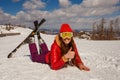 Teenage girl in a red jacket and ski glasses lies in the snow. ski-skier`s photo shoot. ideas photo in the snow