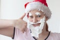 A teenage girl in a Santa hat with a beard, mustache and eyebrows made of shaving foam, a close-up of her face, next to her hand