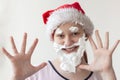A teenage girl in a Santa hat with a beard, mustache and eyebrows made of shaving foam, face close-up, hands with fingers spread