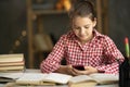 Teenage girl school pupil holding smart phone, studying with book. Focused teen student doing homework using mobile app Royalty Free Stock Photo