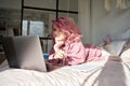 Teenage girl school student pink hair watch online course studying in bed. Royalty Free Stock Photo