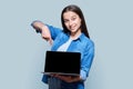 Teenage girl showing blank laptop screen, posing against gray background Royalty Free Stock Photo