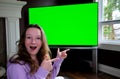 teenage girl sits admiringly in front of a big chroma key tv monitor ad enthusiastically points finger laughs thumbs up