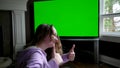 teenage girl sits admiringly in front of a big chroma key tv monitor ad enthusiastically points finger laughs thumbs up