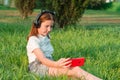 A teenage girl sits in a park on the grass with a smartphone in her hands. 12 year old girl listening to music in headphones Royalty Free Stock Photo