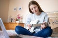 Teenage Girl Sitting On Bed Learning To Play Electric Guitar With Online Lesson On Laptop Computer Royalty Free Stock Photo