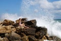 Teenage girl sitting on a stone on the seashore under the splashing waves Royalty Free Stock Photo