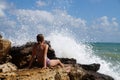 Teenage girl sitting on a stone on the seashore under the splashing waves Royalty Free Stock Photo