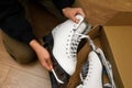 A teenage girl is sitting on the wooden floor in the living room. She holds a figure skate in her hands. Pair of brand new white