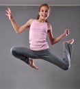 Teenage girl skipping and dancing in studio. Child exercising with jumping on grey background.