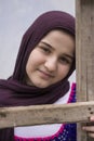 Teenage girl standing in back of wooden ladder wearing traditional knitted cloth with white shawl in front of colored wall