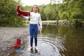 Teenage girl standing in a river wearing socks pours water out of her red wellington boot Royalty Free Stock Photo