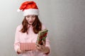 A teenage girl stands at home wearing a Santa hat and opens a Christmas present she is surprised and happy Royalty Free Stock Photo