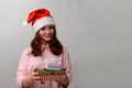 A teenage girl stands at home wearing a Santa hat and smiling, holding gift boxes with gifts Royalty Free Stock Photo