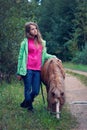 Teenage girl stands with a little horse on the country roadside