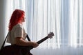 A teenage girl stands at the window with a guitar and is bored without friends