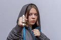 A teenage girl strikes with brass knuckles on a light background, wearing a hoodie with a hood. Concept: street gang of hooligans,