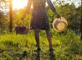 A teenage girl at sunset in a forest field holds a basket with lupines flowers and a straw hat. Impudence and femininity