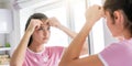 Teenage girl in t-shirt pops pimples reflecting in mirror Royalty Free Stock Photo