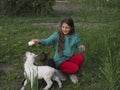A teenage girl takes care of three colorful baby goats in a spring garden on a farm. The concept of unity with nature