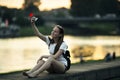 A teenage girl takes a selfie on her phone while sitting on the city embankment. Royalty Free Stock Photo