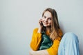 Teenage girl talking on a cellphone and smiles looking at camera. Beautiful girl in yellow sweater and blue jeans holding mobile p