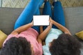 Teenage girl teaching mother to use digital tablet while sitting on sofa at home, copy space