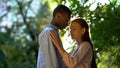 Teenage girl tenderly touching arms of her mixed-race boyfriend at sunny park