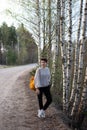A teenage girl travels alone in the spring with a yellow backpack. Sandy road and birch trees. Lifestyle. Vertical photo