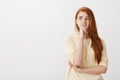 Teenage girl is in trouble, thinking up solution. Portrait of nervous and anxious cute redhead female student holding