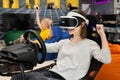 Teenage girl in virtual reality glasses holds the steering wheel and plays a computer game on the console, rejoicing at Royalty Free Stock Photo