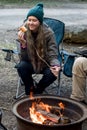 Teenage girl wearing beanie hat eating large marshmallow on a stick roasted over the campfire firepit. Camping family fun Royalty Free Stock Photo