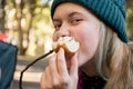 Teenage girl wearing beanie hat eating large marshmallow on a stick roasted over the campfire firepit. Camping family fun Royalty Free Stock Photo