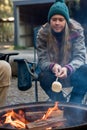 Teenage girl wearing beanie hat roasting large marshmallow on a stick over the campfire firepit. Camping family fun Royalty Free Stock Photo