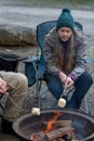 Teenage girl wearing beanie hat roasting large marshmallow on a stick over the campfire firepit. Camping family fun Royalty Free Stock Photo