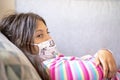 Teenage girl wearing face mask lying in bed checking temperature