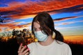 A teenage girl wearing face mask with phone attention sunset background wallpaper Royalty Free Stock Photo